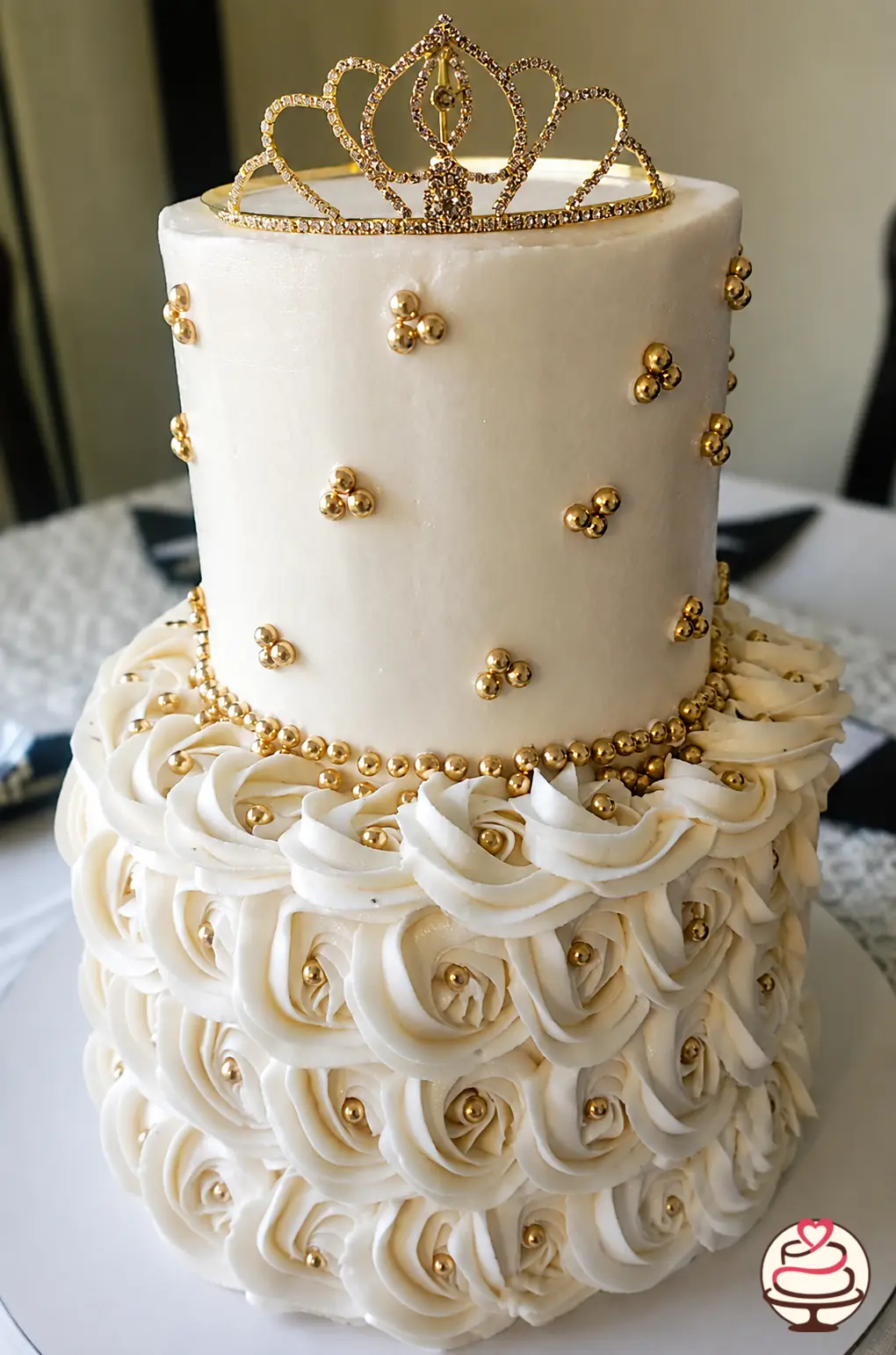 Torta blanca de dos pisos para quince años con rosas de buttercream, perlas doradas y corona