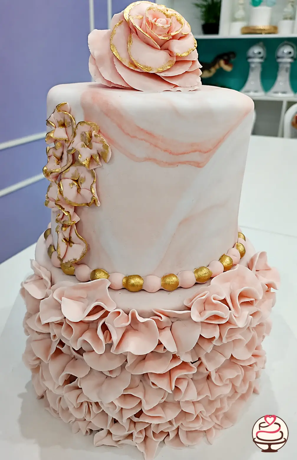 Torta de dos pisos en tonos rosa mármol con flores y volantes de fondant